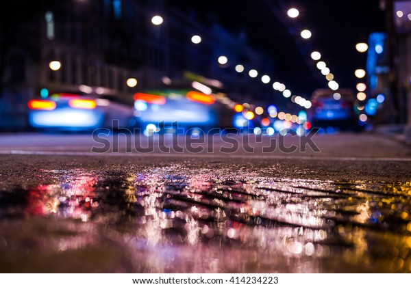Nights lights of the big city, the main city\
street with a racing cars. Close up view from the level of asphalt,\
in blue tones, focus on the\
asphalt