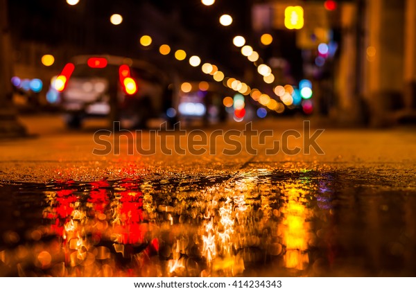 Nights lights of the big city, the main city\
street with parked cars. Close up view from the level of the\
sidewalk, focus on the\
sidewalk