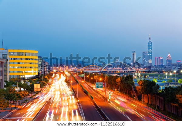 Nightscape of busy car trails on Riverside\
Expressway in Taipei, the vibrant capital city of Taiwan, with 101\
Tower among skyscrapers in XinYi District & beautiful arch\
bridges over Keelung\
River