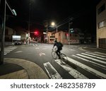 Nighttime city street scene with a cyclist crossing an intersection under streetlights. Capturing the dynamic urban environment and the energy of night life in the city.