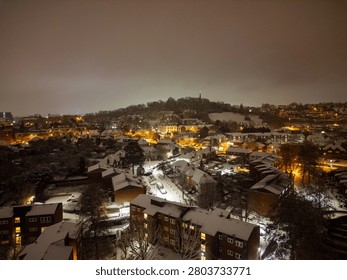 A nighttime cityscape featuring snow-covered rooftops and streets illuminated by warm streetlights, creating a serene winter ambiance.