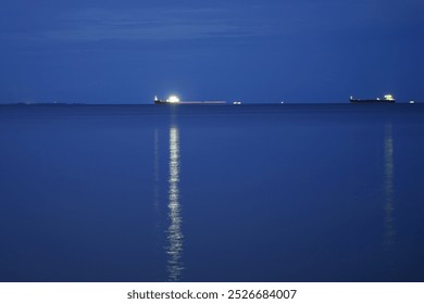 Nighttime coastal landscape with calm water reflecting city lights, industrial skyline silhouette, clear dark sky, tranquil seafront view, urban night scene, waterfront cityscape, peaceful evening  - Powered by Shutterstock