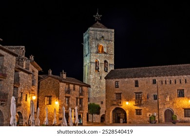 A nighttime view of a historic stone building with a bell tower adorned with a star on top, surrounded by other stone structures and illuminated by warm lights. - Powered by Shutterstock