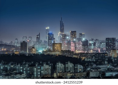 Nighttime view of an illuminated city skyline on a hill, with a variety of different buildings silhouetted against the night sky - Powered by Shutterstock