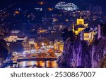 Nighttime view of Tbilisi city centre featuring Mtkvari river, historic Metekhi church and historic quarters.  A vibrant city with illuminated buildings and a flowing river. Capital of Georgia.