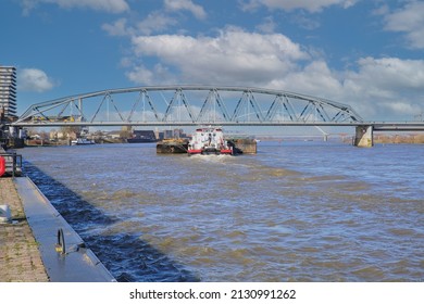 Nijmegen, Netherlands - February 27. 2022: View over river waal with inland waterway vessel on railway truss bridge against blue sky 