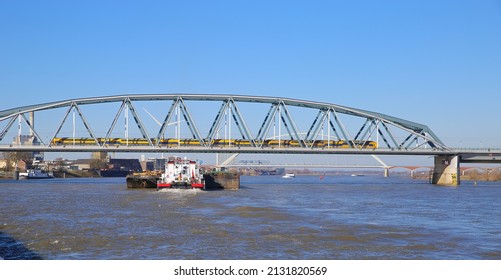 Nijmegen, Netherlands - February 27. 2022: View over river waal with inland waterway vessel on railway truss bridge against blue sky (focus on center)