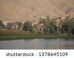 Nile River, Egypt: Two men in a rowboat, farmers with their cattle, date palm trees, houses, and sand dunes along the west bank of the Nile River.