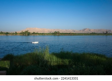 Nile river landscape in Luxor, Upper Egypt, White motorboat on blue water with view of Sahara desert dry mountains and green plantations on river west bank - Shutterstock ID 2241413331