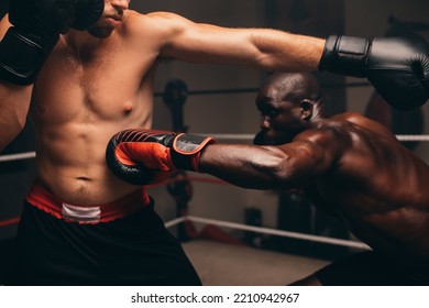 Nimble black athlete striking his challenger in the ribs during a boxing fight. Two athletic young men having a boxing match in a ring. - Shutterstock ID 2210942967