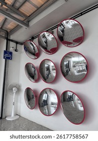 Nine convex mirrors with red frames mounted on a white wall, reflecting indoor surroundings in a modern space.
