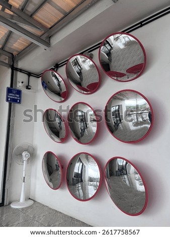 Nine convex mirrors with red frames mounted on a white wall, reflecting indoor surroundings in a modern space.