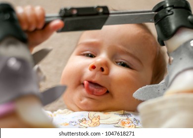 A Nine Month Old Baby With A Tongue Tie And Orthopedic Shoes Lays On Her Back With Her Tongue Sticking Out As Much As Possible As She Holds The Bar Between Her Orthopedic Shoes For A Club Foot.  