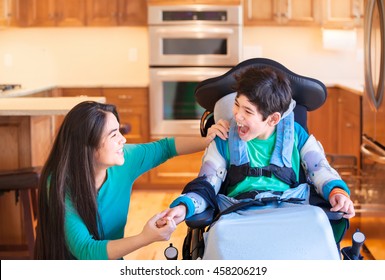 Nine Year Old Disabled Boy In Wheelchair Laughing With Teen Sister In Kitchen