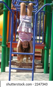 A Nine Year Old Girl Upside Down On Monkey Bars.