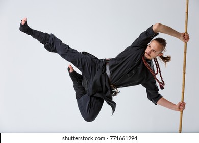 A ninja man holds on to a fighting stick and attacks in a with his foot close-up on a gray background