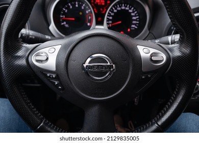 Nissan steering wheel, tachometer and speedometer behind, knees in jeans below - St. Petersburg, Russia, February 2022