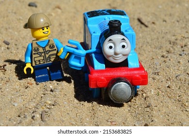 NITRA, SK - APRIL 17, 2022: LEGO City Boy With Baseball Hat Adding Oil To Die Cast Model Of Steam Locomotive Thomas The Tank Engine From Cartoon Of The Same Name, On Sandy Ground In Garden.