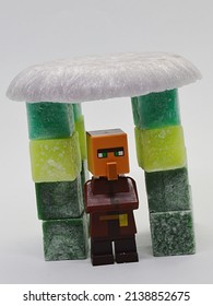 NITRA, SK - MARCH 19, 2022: LEGO Minecraft Figure Of Villager Standing Under The Roof Made Of Melted Scented Pink Wax, Supported By Stearine Wax Cubes Of Various Green Colours.