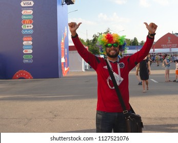 Nizhny Novgorod, Russia-June 24, 2018: Football FIFA fan fest support the national team World Cup. Satisfied fan in colorful wig and glasses raised his hands up, fingers up