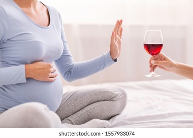 No Alcohol. Unrecognizable Pregnant Girl Refusing To Take Glass Of Wine Sitting On Bed In Bedroom. Cropped