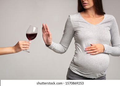 No Alcohol. Unrecognizable Pregnant Lady Gesturing Stop To Offered Glass Of Wine Standing Over Gray Background. Studio Shot, Cropped