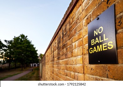 No Ball Games sign on a brick wall.  No ball games are allowed on this part of a residential development. The sign is to stop people kicking balls against the wall. Sign on a wall at sunset with path.