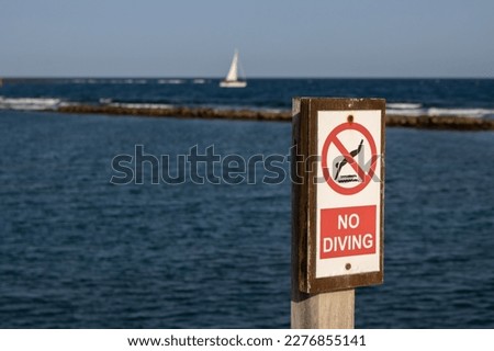 No diving advice on a wooden board. Atlantic ocean and a sailing boat in the blurry background. Blue sky. Fuerteventura, Canary Islands, Spain, Europe.
