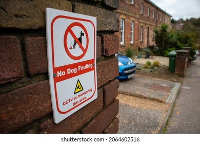 No dog fouling and CCTV monitoring sign on a residential street with a row of Victorian red brick houses and front gardens in the background