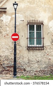 No Entry Roadsign Hanging On Street Lamp Post Against Background Of Old Weathered House 