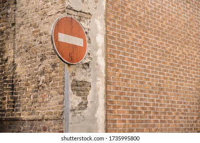 
No Entry Sign Stands Next To An Old House With Red Brick Wall