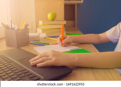 No Face Shot Of A Child Boy Typing On The Keyboard Of His Laptop Computer While Doing Homework, Studying Online At Home At Wooden Table Near The Window