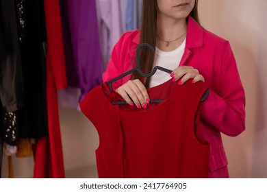 No face, a woman in a pink suit and pink nails chooses what to wear. Hanger with a red dress, for a holiday. Decluttering, wardrobe analysis with a stylist, outfit of the day - Powered by Shutterstock