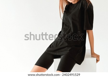 No face woman wears an oversized black shirt. dark streetwear outfit young girl. Black t-shirt mock-up isolated horizontal studio shot against a white wall.