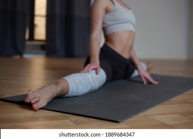 No Face Young Woman Doing Twine Stretching On Youga Mat In Room With Wooden Floor And White Walls. Selective Focus