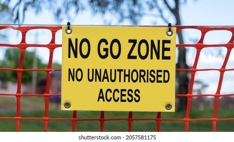 No Go Zone, No Unauthorised Access Sign In Front Of Bright Orange Safety Barrier Mesh. Bright Yellow Safety Sign Outdoors. Control Concept.