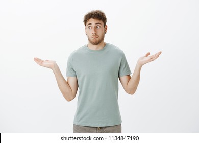 No idea how it happened. Portrait of awkward unaware funny guy in t-shirt and earrings, making clueless expression and shrugging with spread palms, being questioned and confused with question