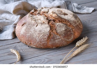 No knead handmade loaf on cutting board on wood with linen towel, spelt ears. German Bauernbrot means Rustic Farmers Bread in English. Wholemeal rye wheat bread baked in Duch oven at home. - Shutterstock ID 1910606857