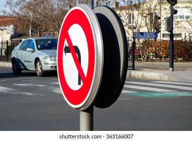 No left turn sign at intersection in center town with car in background