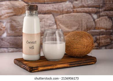 NO LOGO. NO TRADEMARK. Coconut milk in a bottle and a glass on a background of coconut on a wooden cutting board. High quality photo. Vegan-friendly drink