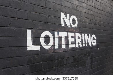 No loitering warning sign painted in large letters on a black painted brick wall.
