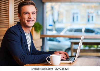 No minute without my laptop. Handsome young man working on laptop and smiling while enjoying coffee in cafe - Powered by Shutterstock