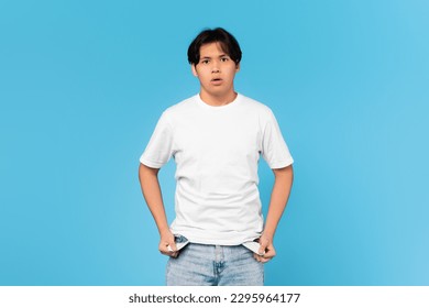 No Money. Unhappy Japanese Teen Boy Showing Empty Pockets Having Financial Problems Looking At Camera In Shock Posing Standing Over Blue Studio Background. Crisis Concept - Powered by Shutterstock