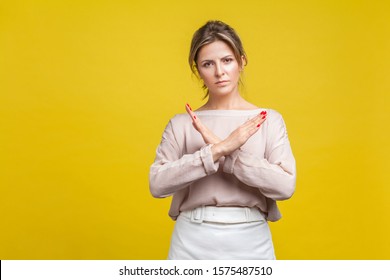 No More, This Is The End. Portrait Of Serious Stubborn Young Woman With Fair Hair In Casual Blouse Standing Showing Closed Gesture With Crossed Hands. Indoor Studio Shot Isolated On Yellow Background