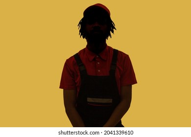 No name, anonymous hiding face in shadow, human identity. Silhouette portrait of male person wearing overalls, standing calm alone in darkness. Indoor studio shot isolated on yellow background.