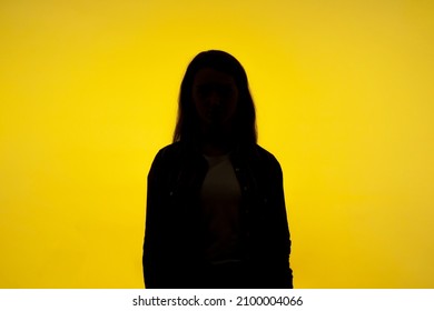 No name, anonymous person hiding face in shadow, human identity. Silhouette portrait of unknown woman standing alone, indoor studio shot, isolated on yellow background