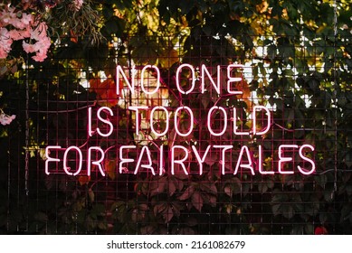 No one is too old for fairytales - neon sign on a wall at an outdoor wedding party. Love concept