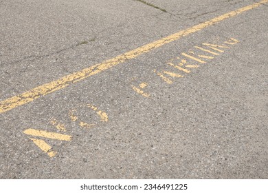 no parking caption print text writing in yellow below line on pavement, worn and faded, shot on angle going diagonal