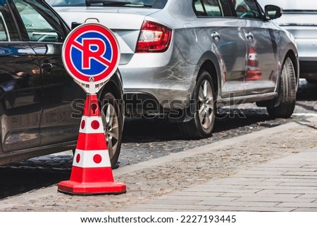 No parking or parking forbidden or prohibited sign with a red and white cone next to a some parked cars