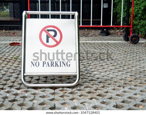No parking sign on stainless\
steel board. Symbol of no parking on cememt block in public\
park.